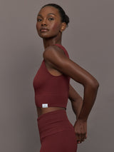 Model wears sports bra in Terracotta with a high neckline and a subtle patterned detailing in the center front.

