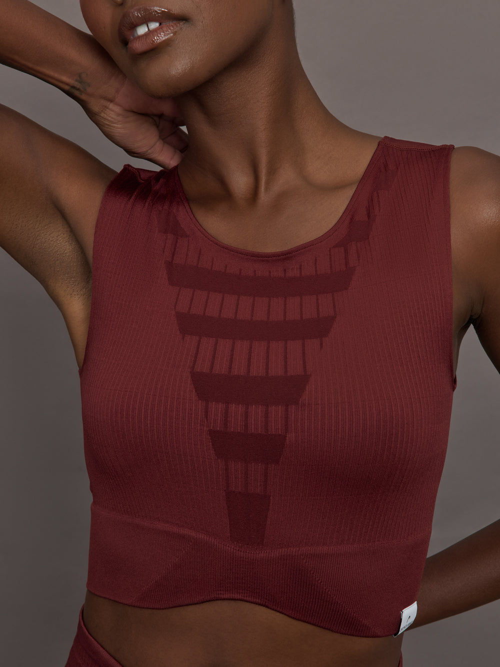 Model wears sports bra in Terracotta with a high neckline and a subtle patterned detailing in the center front.
