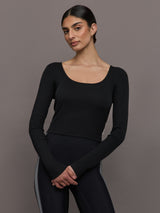 Model wears a long sleeved scoop neck black crop top. 