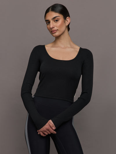 Model wears a long sleeved scoop neck black crop top. 