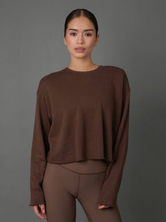 Model wears a french terry crew sweatshirt in Carafe color way against a grey background. 