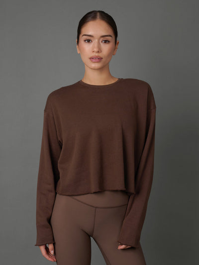 Model wears a french terry crew sweatshirt in Carafe color way against a grey background. 