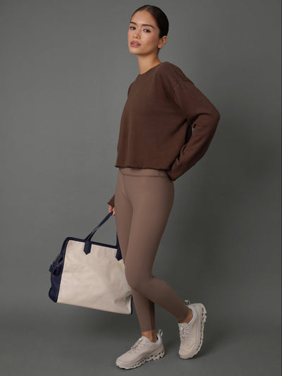 Model wears a french terry crew sweatshirt and leggings in Carafe color way against a grey background. 