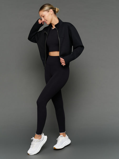 Model is wearing Melt scallop edge legging in black white styled with jacket, full body view.