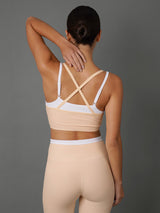 A woman shown from the back wearing a beige sports bra and matching leggings against a plain gray studio background.