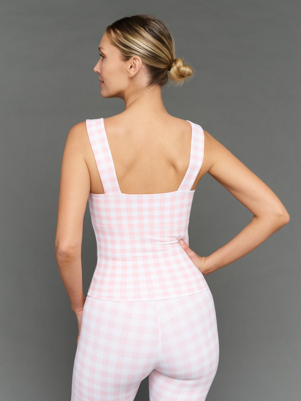 Model wears a pink gingham tank top against a grey background, back view
