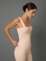 A woman modeling a nude-beige Ribbed Tank with integrated leggings against a solid dark gray studio background.