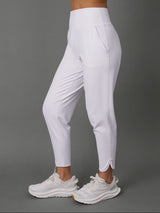 A model wearing a matching white activewear set consisting of a sports bra and high-waisted leggings with side pockets, paired with white sneakers, shown from the waist down against a solid gray studio background.
