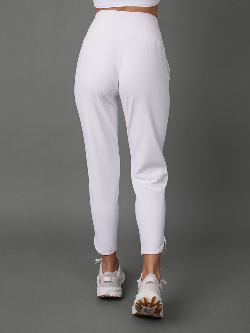 White activewear set featuring a one-shoulder crop top and high-waisted cropped leggings, shown from the back on a model against a solid gray studio background.