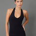 A woman modeling a black halter-neck bodysuit with matching black leggings against a solid gray studio background.