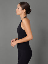 A woman in side profile wearing a black sleeveless athletic jumpsuit against a solid gray studio background.