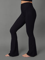 Model wears black bootcut leggings against a grey background, side view. 