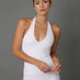 A woman modeling a white sleeveless halter-neck top and matching white pants against a solid dark gray studio background.