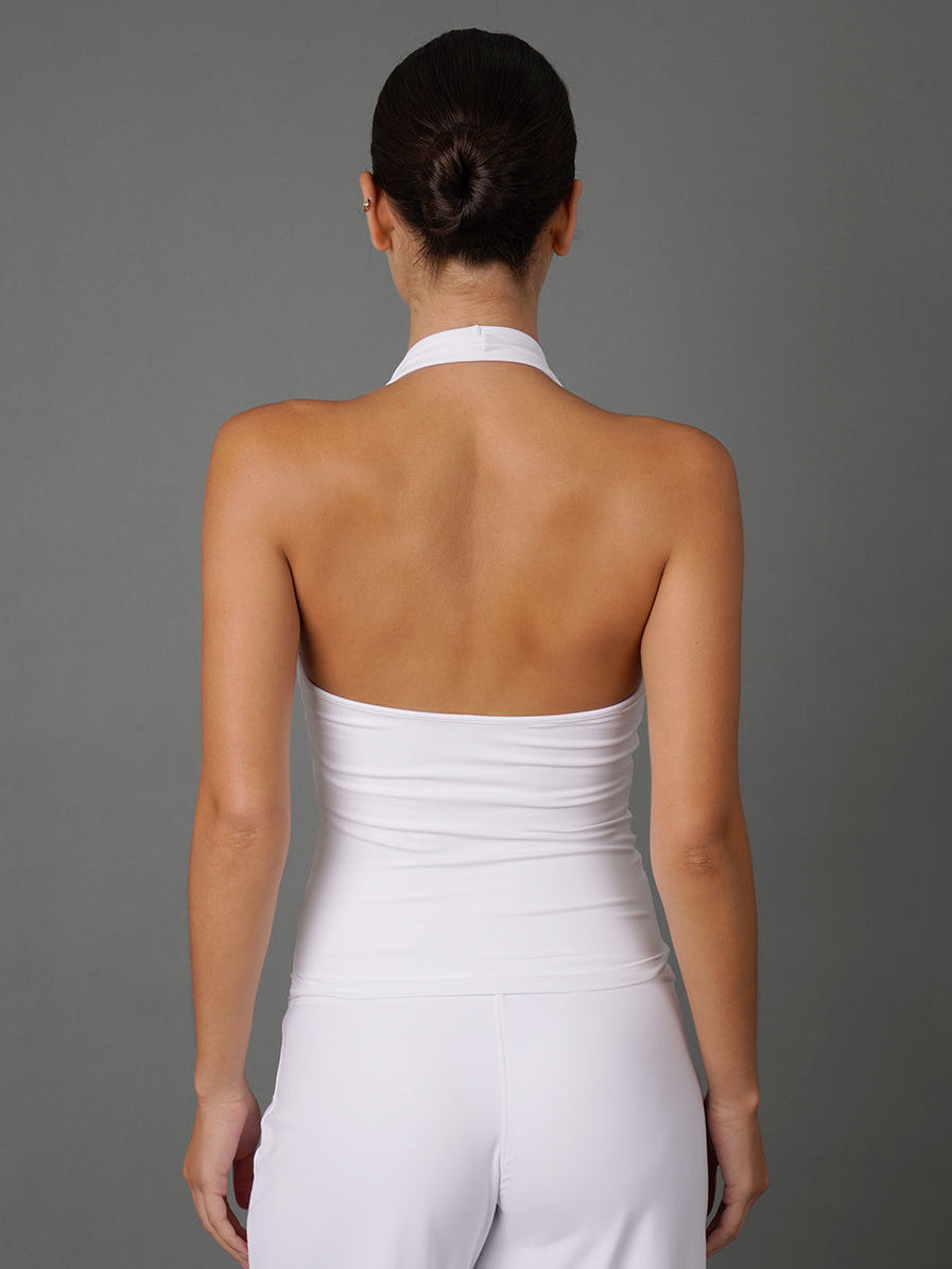 A woman viewed from the back wearing a white halter-style strapless top and matching white pants against a plain gray studio background.