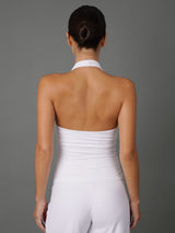 A woman viewed from the back wearing a white halter-style strapless top and matching white pants against a plain gray studio background.