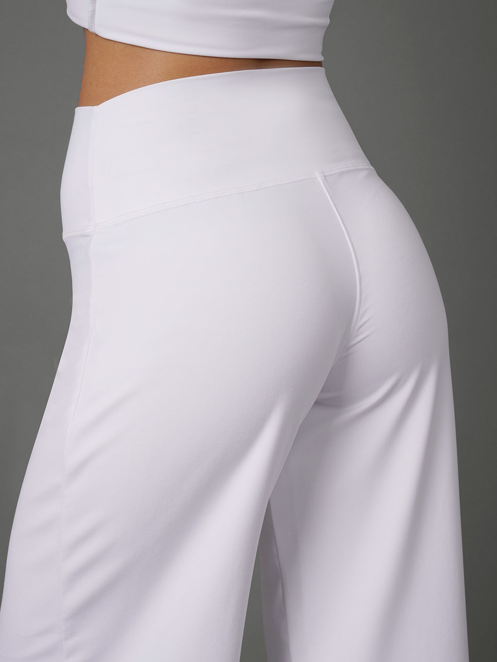 White high-waisted athletic pants shown on a model from a rear three-quarter angle against a solid gray background.