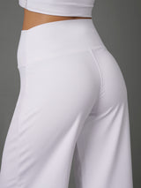 White high-waisted athletic pants shown on a model from a rear three-quarter angle against a solid gray background.