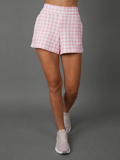 Model wears Pink Gingham french terry sweat shorts against a grey background, waist down shot. 