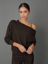 A woman modeling a dark brown off-the-shoulder long-sleeve sweatshirt with a thin black underband and black leopard-print leggings, set against a solid gray studio background.