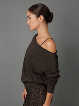 A woman in side profile wearing a dark brown cold-shoulder knit sweater and leopard-print pants against a solid gray studio background.