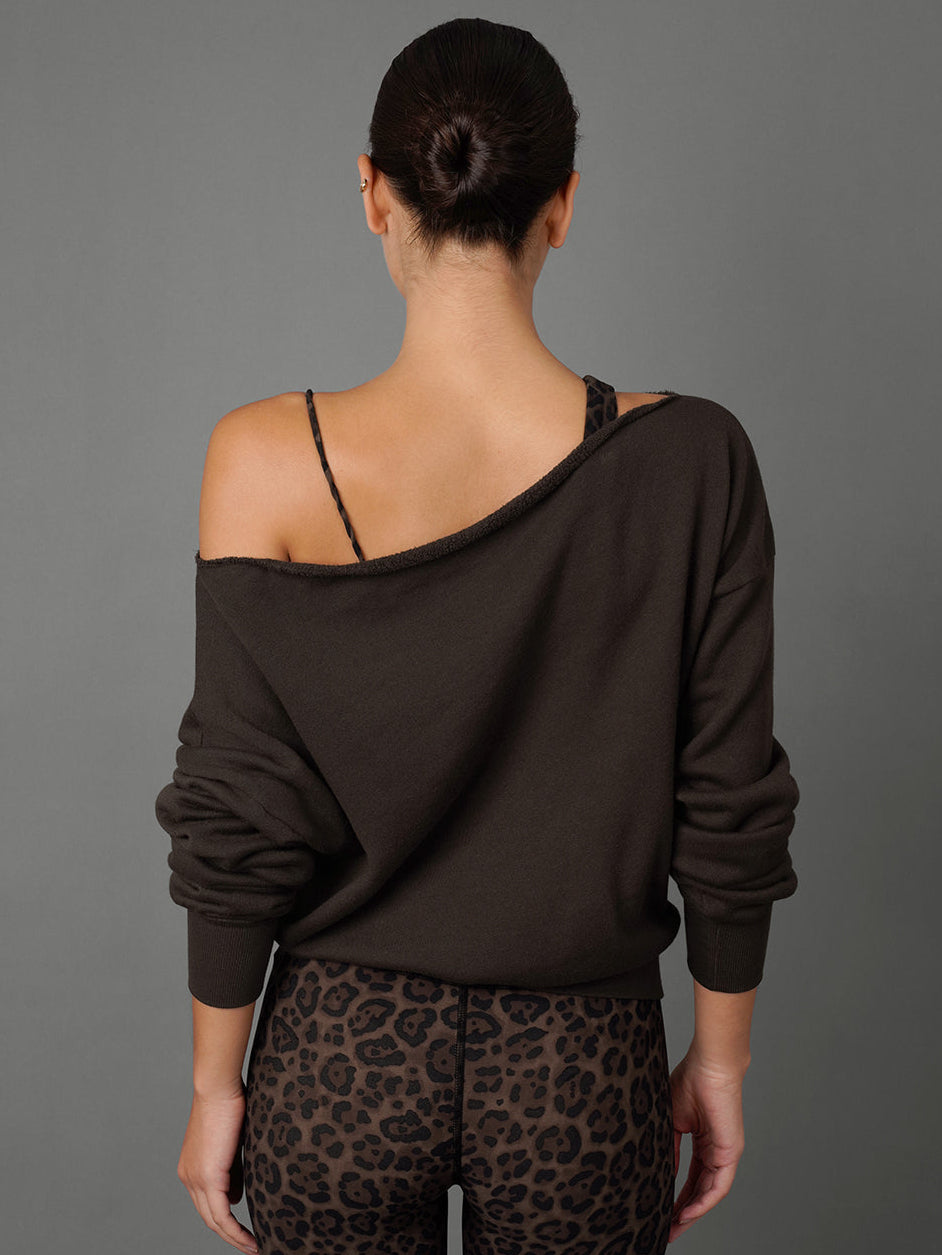 A woman shown from the back wearing a dark brown off-the-shoulder long-sleeve top and leopard-print leggings against a solid gray studio background.