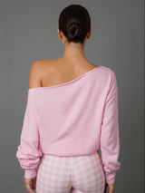 A woman shown from the back wearing a light pink off-the-shoulder long-sleeve top and pink-and-white gingham pants against a solid gray studio background.