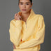 Model wears an interlock half zip sweatshirt in yellow against a grey backdrop. 