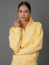 Model wears an interlock half zip sweatshirt in yellow against a grey backdrop. 