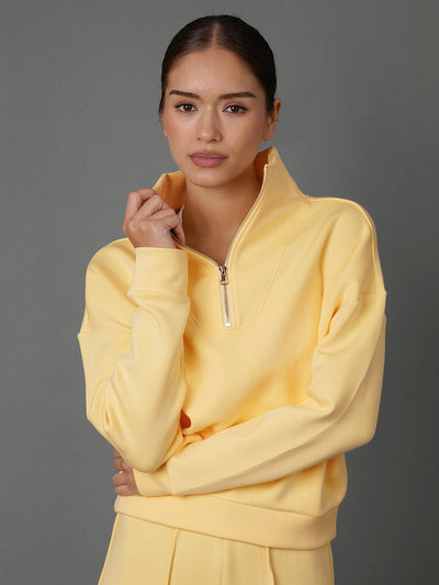 Model wears an interlock half zip sweatshirt in yellow against a grey backdrop. 
