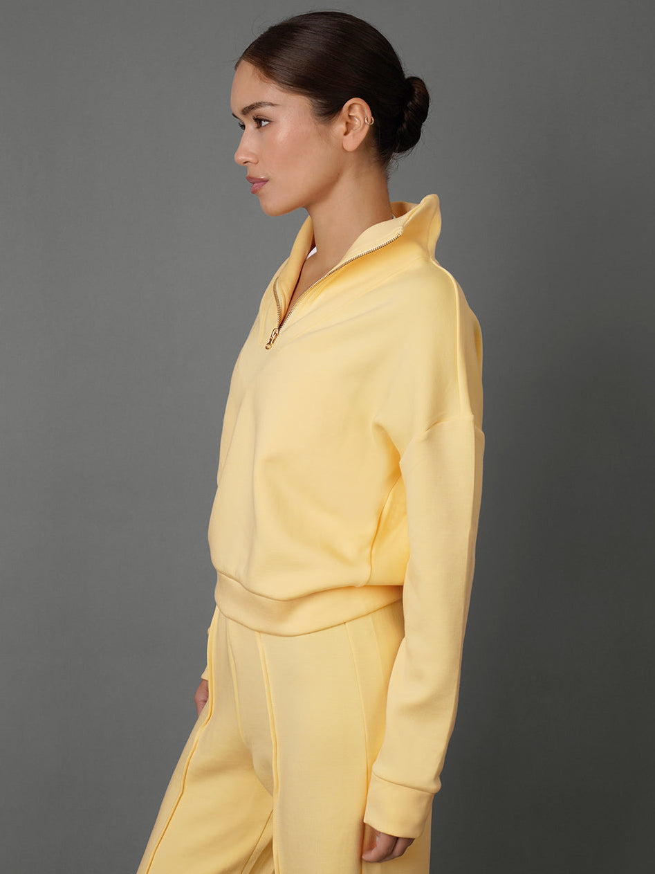 Model wears an interlock half zip sweatshirt in yellow against a grey backdrop / side view