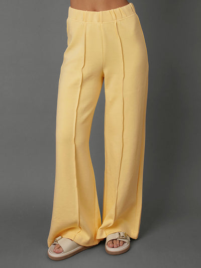 Model wears yellow interlock pants against a grey background.
