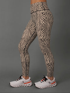 Close up shot / side view of a model from the waist down wearing Zebra print leggings against a grey background