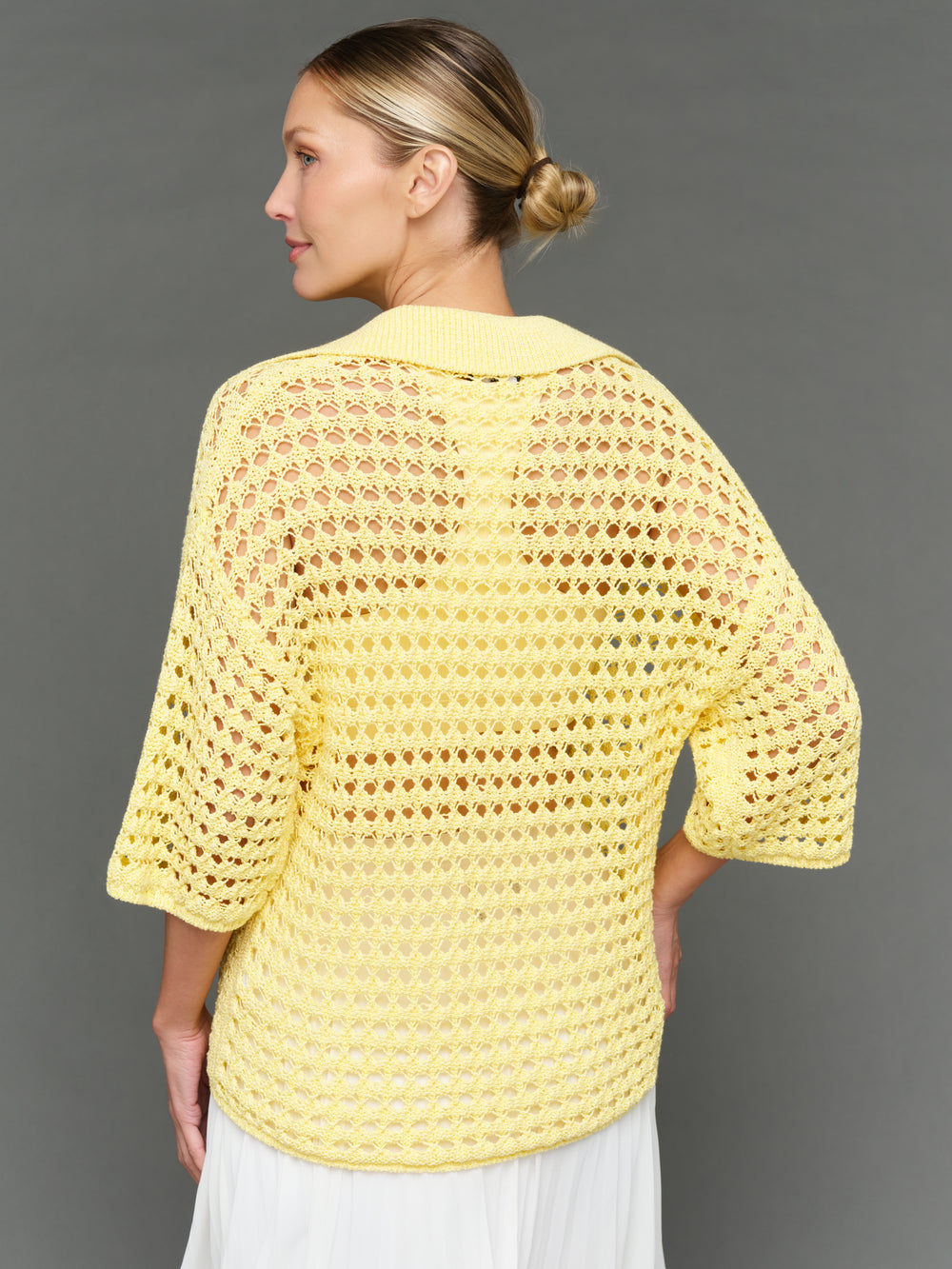 Model is wearing open knit polo sweater pale banana, back view.
