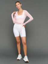 Woman wearing a pink knit top and white shorts on a gray background