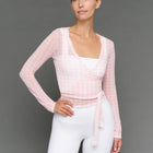 Model wearing a light pink long-sleeve top and white shorts against a gray background