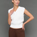 Woman wearing a white sleeveless top and brown pants against a gray background