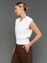 Woman wearing a white textured top and brown pants against a gray background