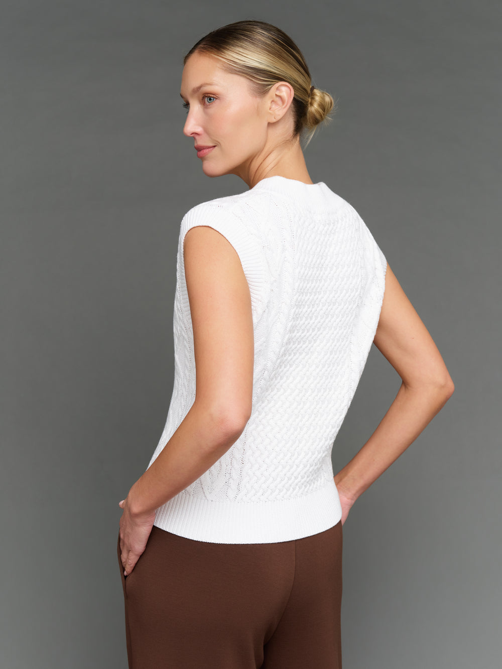 Woman wearing a white sleeveless top against a gray background