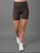 A model from the waist down wearing high-waisted leopard print athletic shorts, a white crop top, and white sneakers against a solid gray studio background.