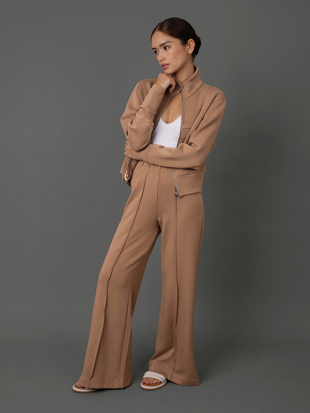 Model wears and interlock jacket in Caribou, white tank top, and interlock pants in Caribou against a grey background.