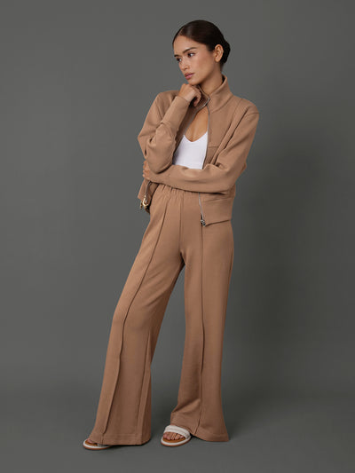 Model wears and interlock jacket in Caribou, white tank top, and interlock pants in Caribou against a grey background.