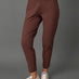 A model wearing a matching brown activewear set consisting of a cropped tank top and high-waisted leggings, paired with white sneakers, against a solid gray studio background.