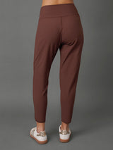A model shown from the back wearing a matching brown activewear set, featuring high-waisted leggings and a cropped sports bra, paired with white sneakers, against a solid gray studio background.